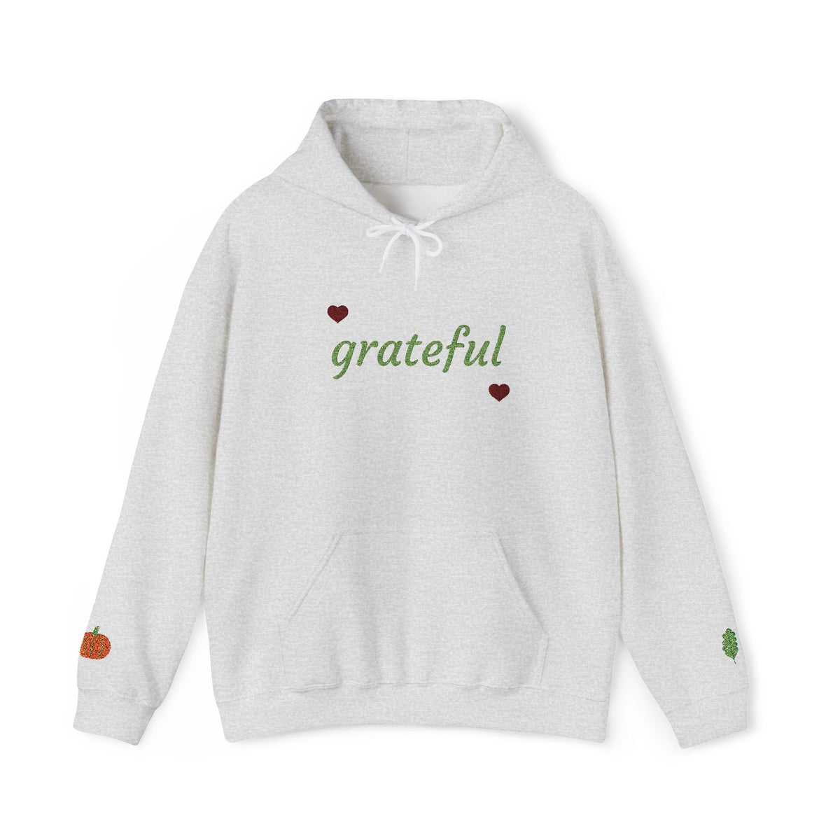 A light heather gray pullover hoodie with 'grateful' written in green script across the chest, accented by two small red hearts. The hoodie features a white drawstring hood, a front kangaroo pocket, a small orange pumpkin graphic on the left sleeve, and a small green leaf graphic on the right sleeve.