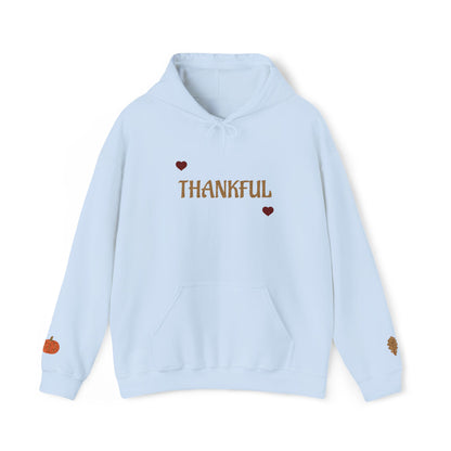 A light blue pullover hoodie with 'THANKFUL' printed in brown across the chest, flanked by two small red hearts. The hoodie features a drawstring hood, a front kangaroo pocket, a small orange pumpkin graphic on the left sleeve cuff, and a small brown leaf graphic on the right sleeve cuff, shown against a plain white background.